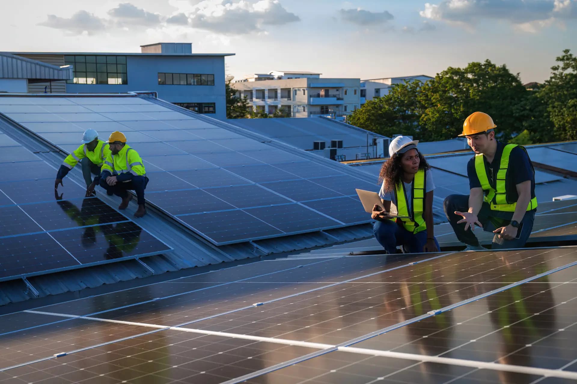 Vier Techniker in Warnwesten begutachten Solarmodule auf einem Metalldach während der Installation bei Tageslicht.